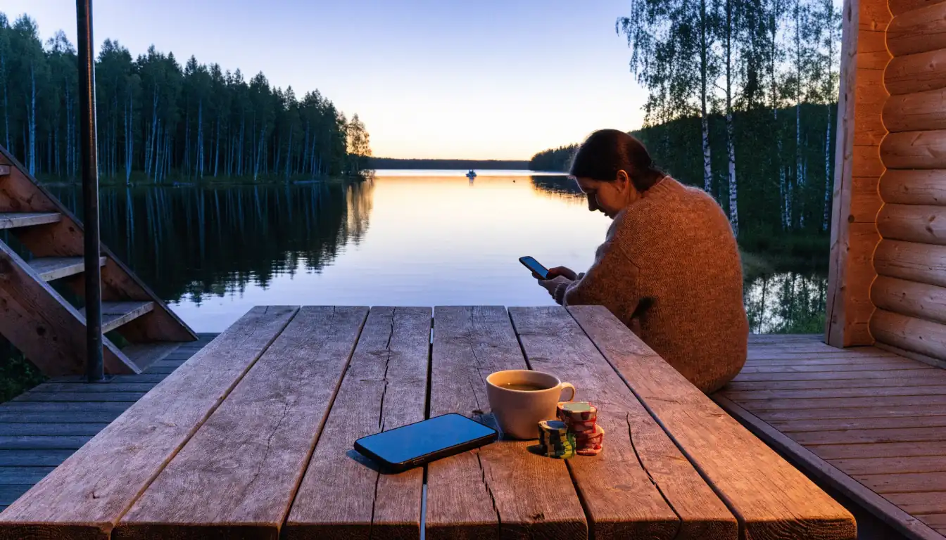 Suomalainen mökki järven rannalla, puhelin ja pelimerkit puisella pöydällä